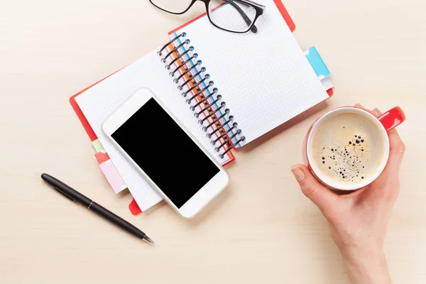 ビジネス デスクの上のコーヒー カップを保持している女性の手 メモ帳や表のスマート フォン コピー スペース平面図 — ストック写真