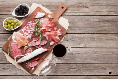 Salam, dilimlenmiş jambon, sosis, jambon, pastırma, tost, zeytin. Et meze tabağı ve ahşap masa üzerinde kırmızı şarap. Kopya alanı ile Üstten Görünüm