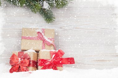 Noel hediye kutuları ve köknar Dalı tarafından ahşap duvar önünde kar kaplı ağaç. Tebrik metninizi ile alan