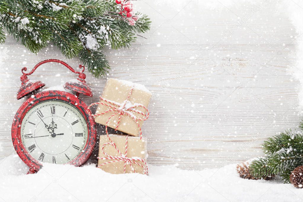 Christmas gift boxes, alarm clock and fir tree branch covered by snow in front of wooden wall. View with copy space