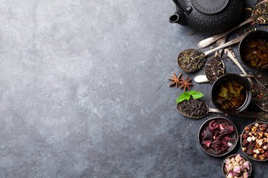 Çaydanlık, çay ve otlar karanlık taş zemin üzerine kaşıklarla kaseler. Kopya alanı ile üstten görünüm
