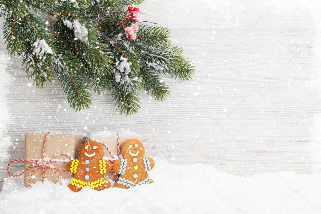 Christmas gift boxes, gingerbread cookies and fir tree branch covered by snow in front of wooden wall. View with copy space