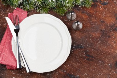 Ahşap arka plan üzerinde kar tarafından Noel tablo ayarını boş tabak, çatal bıçak ve köknar ağacı dalı ile kaplı. Selam yeri olan üstten görünüm