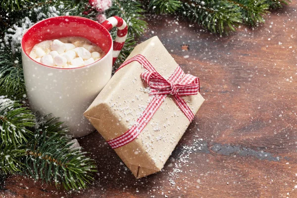 クリスマス ギフト ボックス 木製の背景に雪で覆われて マシュマロとモミの木の枝とホット チョコレートのカップ あなたの挨拶のためのスペースとクリスマス背景 — ストック写真