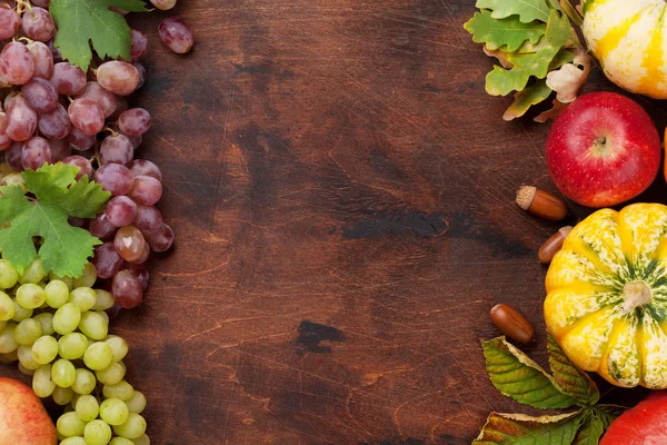 stock image Autumn backdrop with pumpkins, apple, grapes and colorful leaves on wooden background. Top view with space for your text