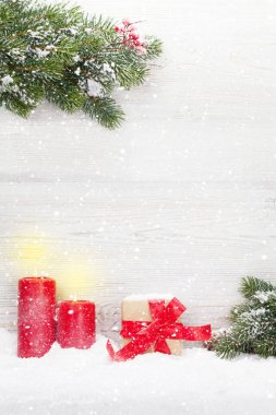 Noel hediye kutusu, mumlar ve köknar ağacı dalı tarafından ahşap duvar önünde kar kaplı. Xmas zemin alan selam ile