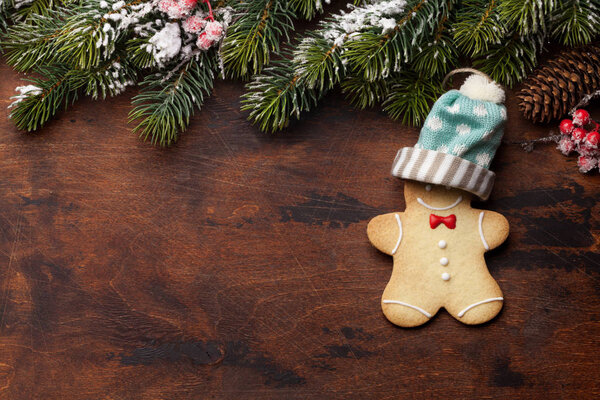 Christmas greeting card with gingerbread cookie and xmas fir tree branch over wooden backdrop. Top view with space for your greetings