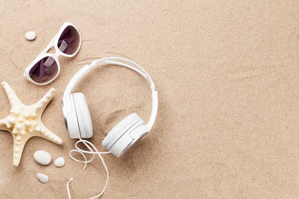 Travel vacation and music concept with headphones, sunglasses, seashells on sand backdrop. Top view with copy space. Flat lay