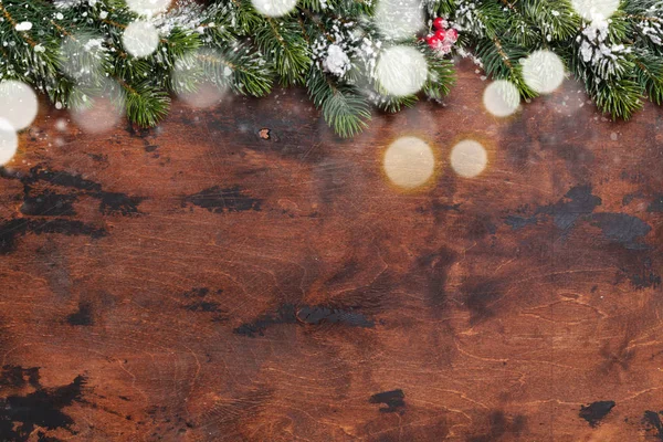 Christmas fir tree branch covered by snow on wooden background. Top view xmas backdrop with space for your greetings