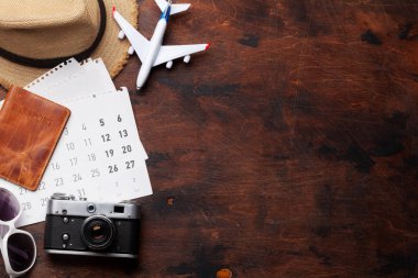 Tatil arka plan kavramı ile güneş gözlüğü, şapka, fotoğraf makinesi, pasaport, uçak oyuncak ve takvim ahşap zemin üzerinde seyahat. Üstten görünüm kopya alanı ile. Düz yatıyordu
