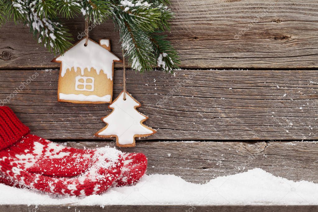Christmas card with gingerbread cookies, mittens and fir tree branch covered by snow in front of wooden wall. With space for your greetings