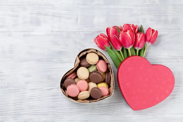 赤いチューリップの花の花束と木製の背景にハートのギフト ボックスのマカロン バレンタインのグリーティング カード あなたの挨拶のためのスペースのトップ ビュー — ストック写真