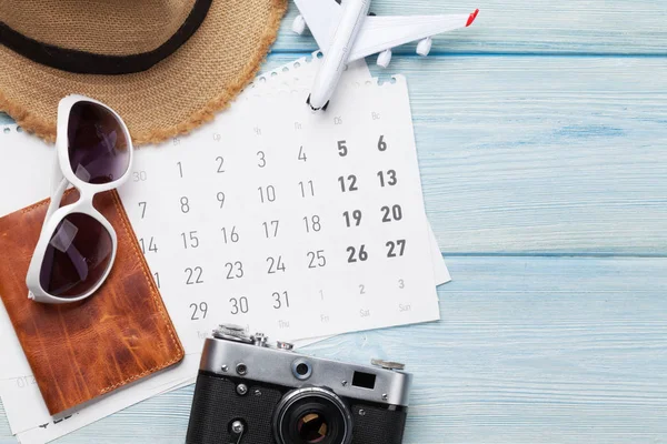 Travel vacation background concept with calendar, sun hat, camera, passport, airplane toy and sunglasses on wooden backdrop. Top view. Flat lay