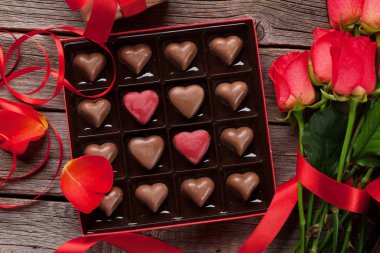 Sevgililer günü tebrik kartı kırmızı gül ve kalp şeklinde çikolata ahşap arka plan üzerinde. Üstten Görünüm