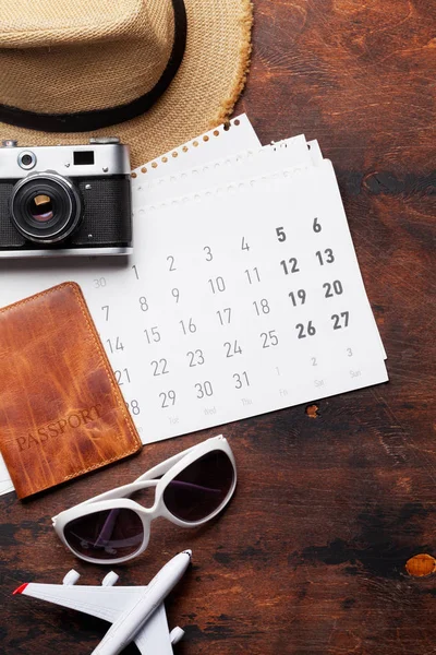 Travel vacation background concept with calendar, sun hat, camera, passport, airplane toy and sunglasses on wooden backdrop. Top view. Flat lay