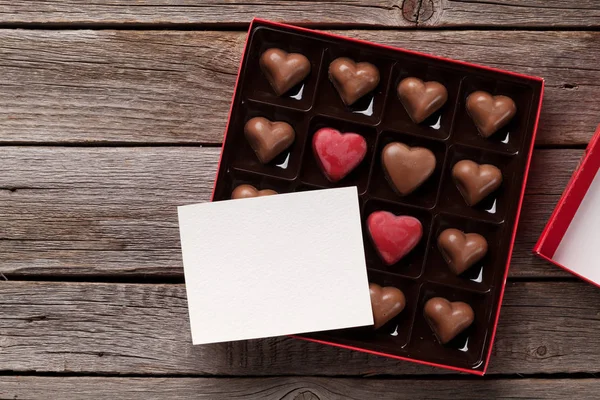 木製のテーブルのボックスにチョコレートの心とバレンタインデーのグリーティング カード あなたの挨拶のためのスペースのトップ ビュー — ストック写真