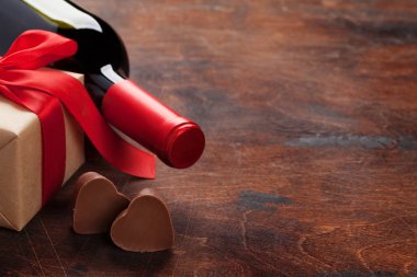 Sevgililer günü tebrik kartı ahşap arka plan üzerinde şarap şişesi, çikolata kalpleri ve hediye kutulu. Selam ile alan