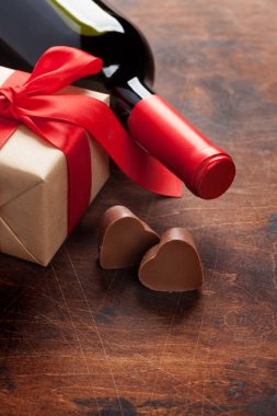 Sevgililer günü tebrik kartı ahşap arka plan üzerinde şarap şişesi, çikolata kalpleri ve hediye kutulu. Selam ile alan