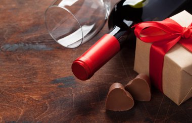 Sevgililer günü tebrik kartı ahşap arka plan üzerinde şarap şişesi, çikolata kalpleri ve hediye kutulu. Selam ile alan