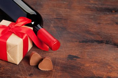 Sevgililer günü tebrik kartı ahşap arka plan üzerinde şarap şişesi, çikolata kalpleri ve hediye kutulu. Selam ile alan