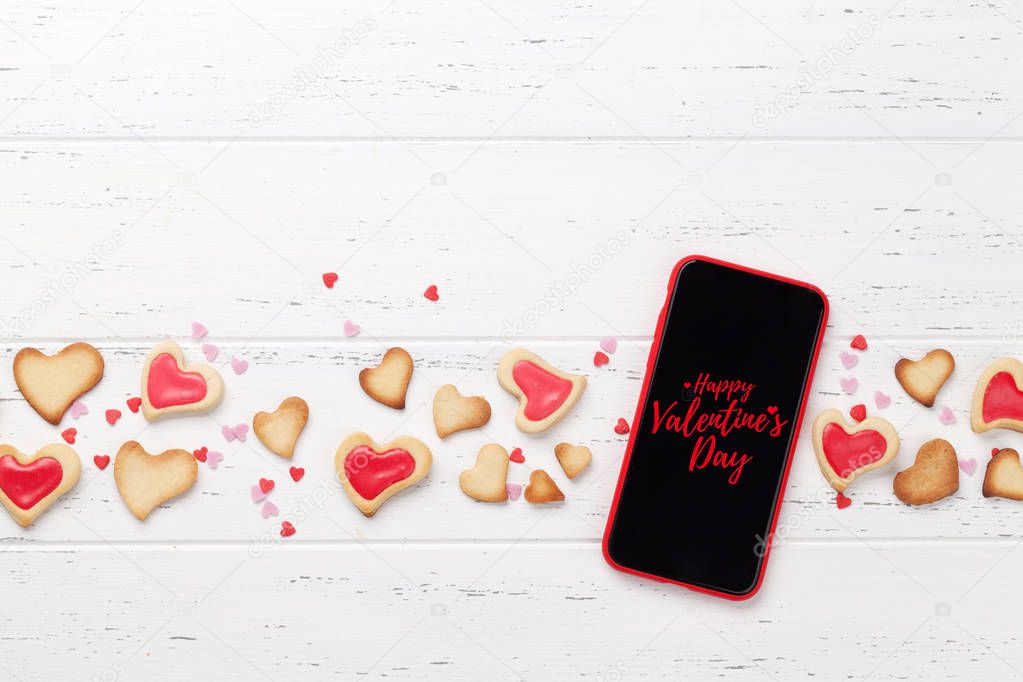 Valentine's day greeting card with heart shaped cookies and smartphone on wooden background. Top view with space for your greetings or smart phone app. Flat lay