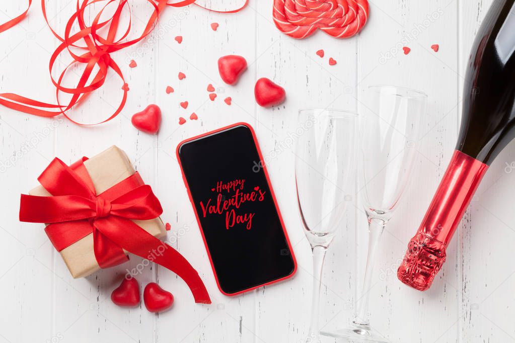 Valentine's day greeting card with gift box, champagne and smartphone on wooden background. Top view with space for your greetings or smart phone app. Flat lay