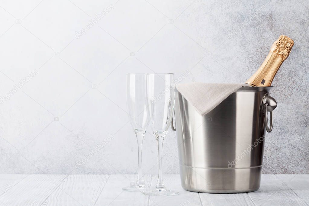 Champagne bottle in bucket and glasses in front of stone wall. With space for your text