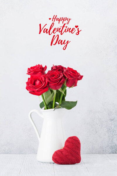 Открытка на день Святого Валентина с букетом из красных роз и вязаным сердцем перед каменной стеной
