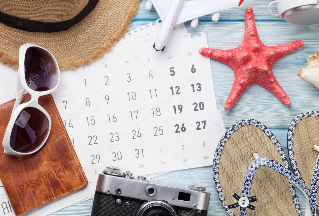 Travel vacation background concept with calendar, sun hat, camera, passport, airplane toy and starfish on wooden backdrop. Top view. Flat lay