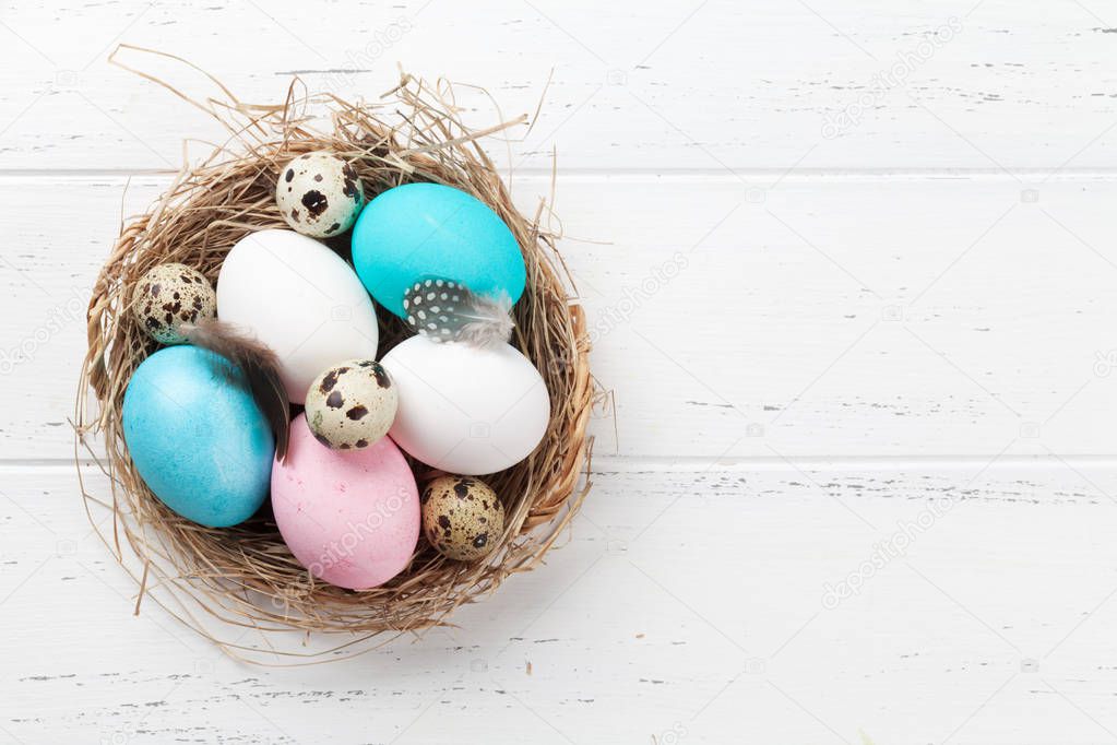 Easter greeting card with colorful eggs in nest on white wooden table. Top view with space for your greetings