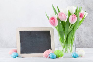 Lale çiçek ve Paskalya yumurta Paskalya tebrik kartı. Selam için kara tahta ile taş duvarın önünde