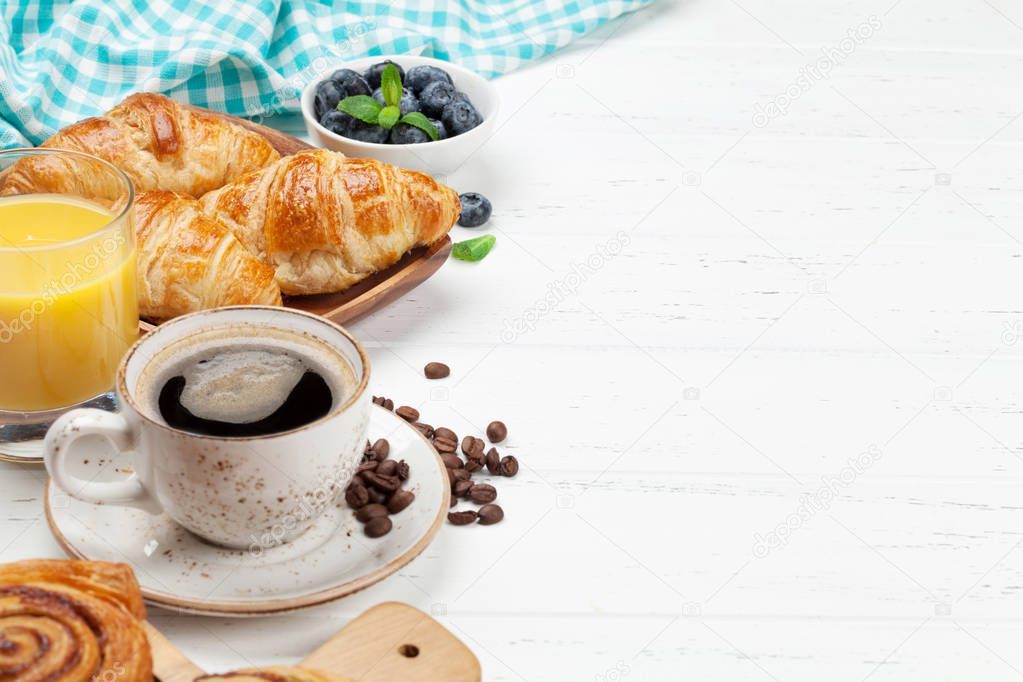 Coffee, croissants, orange juice, cinnamon rolls and berries breakfast. On wooden table. With copy space for your text