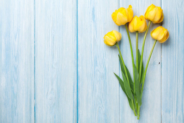 Yellow tulips on blue wooden table. Top view with space for your text