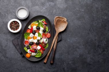 Salatalık, domates, biber, marul, soğan, beyaz peynir ve zeytin taş arka plan üzerinde beyaz plaka ile Yunan salatası