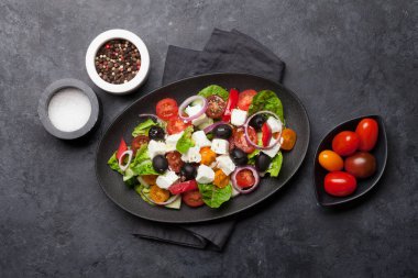 Salatalık, domates, biber, marul, soğan, beyaz peynir ve zeytin taş arka plan üzerinde beyaz plaka ile Yunan salatası