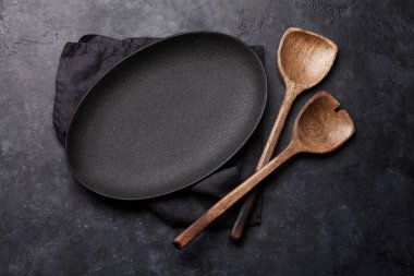 Ahşap mutfak aletleri ve karanlık taş zemin üzerine boş levha 