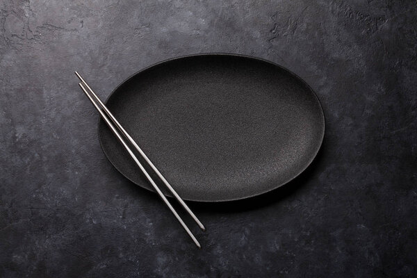 Empty plate and chopsticks over black textured table