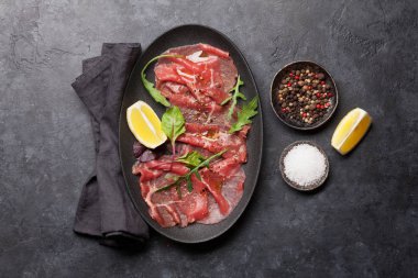 Mermer Dana carpaccio roka yeşil yaprakları ve limon taş zemin üzerine ile 