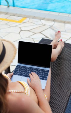 Yüzme Havuzu yakındaki iş için dizüstü bilgisayar kullanan genç kadın