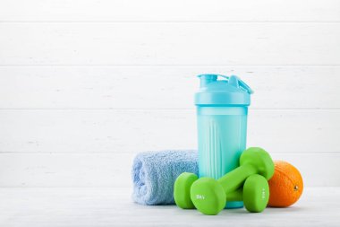Beyaz ahşap masada dumbbells, turuncu ve içecek şişesi
