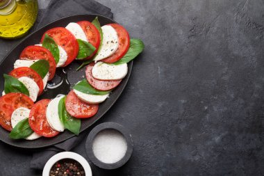 Olgun domates, fesleğen yaprakları ve taş arka planda mozzarella peyniri ile geleneksel Caprese salatası