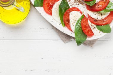 Beyaz ahşap arka planda zeytin yağı ile giyinmiş İtalyan Caprese salatası 