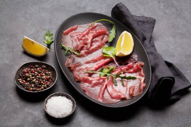 Mermer Dana carpaccio roka yeşil yaprakları ve limon taş zemin üzerine ile 