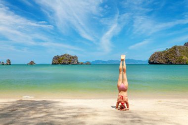 Genç bir kadın plajda yoga yapıyor.