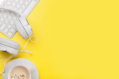 Kahve fincanı, kulaklık ve bilgisayar ile sarı ofis işyeri.