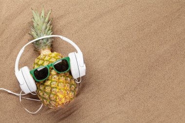 Olgun ananas, güneş gözlüğü ve kulaklıkla sıcak kumsalda fotokopi alanı ile. Seyahat ve tatil konsepti. Üst görünüm düzlüğü