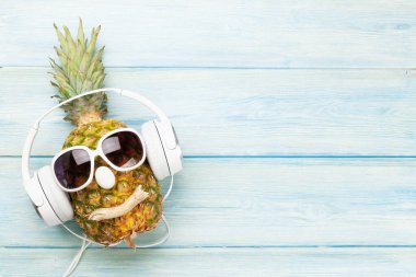 Mavi ahşap arka planda, güneş gözlüklü ve kulaklıklı olgun ananas. Seyahat ve tatil konsepti. Üst görünüm düzlüğü kopyalama alanı ile yatıyordu