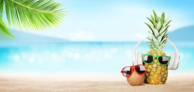 Parlak dalgalı tropikal deniz, güneş gözlüklü ananas ve sıcak kumsalda kulaklık. Kopya alanı ile seyahat ve tatil kavramı