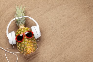 Olgun ananas, güneş gözlüğü ve kulaklıkla sıcak kumsalda fotokopi alanı ile. Seyahat ve tatil konsepti. Üst görünüm düzlüğü