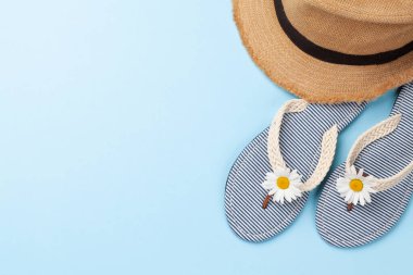 Yaz tatili eşyaları ve aksesuarları. Mavi arka planda terlik ve güneş şapkası. Üst görünüm düzlüğü kopyalama alanı ile yatıyordu